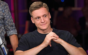 Felix Kroos sitzt mit gefalteten Händen in einer Talkshow