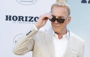 Kevin Costner im beigen Anzug schielt über seine Sonnenbrille hinweg