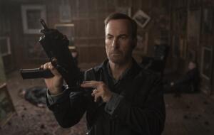 Schauspieler Bob Odenkirk verkörpert Nobody im gleichnamigen Film und hält eine automatische Waffe, einsatzbereit, hoch