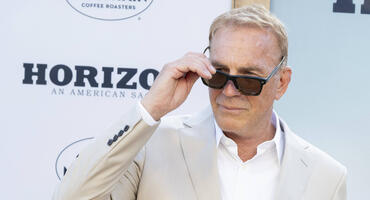 Kevin Costner im beigen Anzug schielt über seine Sonnenbrille hinweg