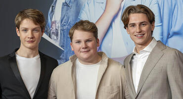 Levi Brandl, Nevio Wendt und Julius Weckauf stehen nebeneinander vor der Fotowand der Premiere der drei Fragezeichen und lächeln in die Kamera.