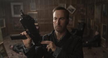 Schauspieler Bob Odenkirk verkörpert Nobody im gleichnamigen Film und hält eine automatische Waffe, einsatzbereit, hoch